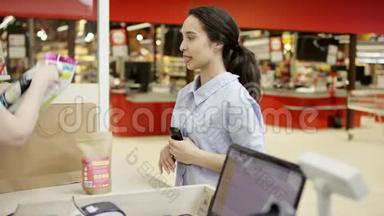漂亮的微笑女孩在超市的收银台等待收银员把她的东西打包成纸
